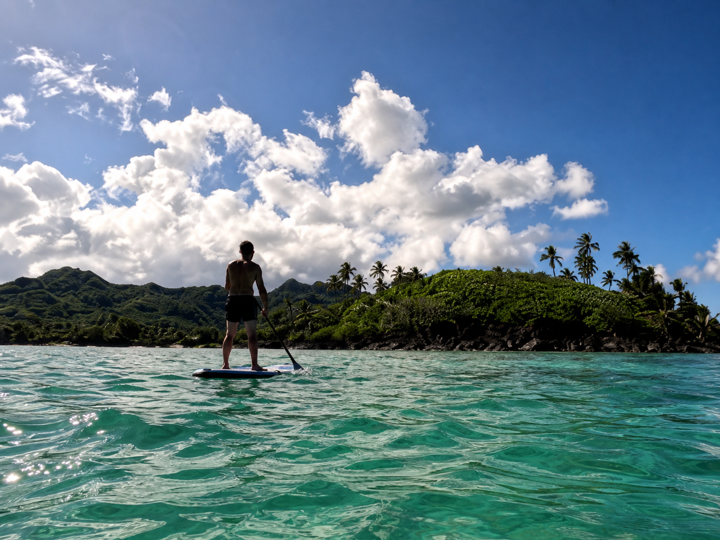 Simon stand-up paddleboarding across a Rarotonga lagoon